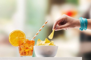 Barda kokteyl içip cips yiyen genç bir kadın.