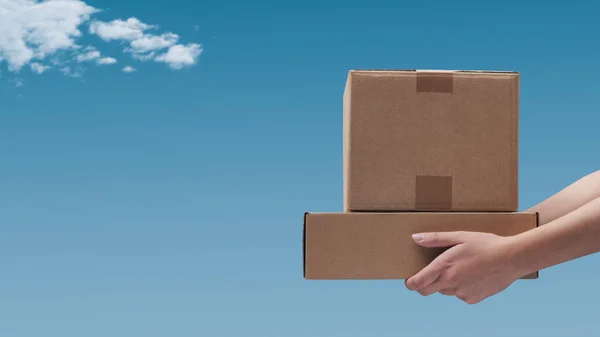 Hands holding delivery boxes and blue sky in the background: delivery and shipping concept
