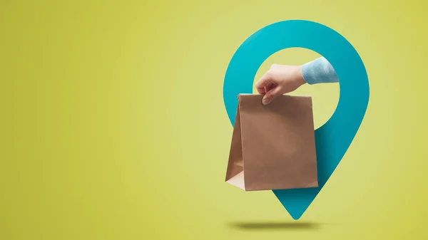 Hand holding a food delivery bag and location pin, fast food delivery concept