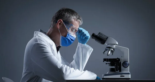 Wetenschapper Met Gezichtsmasker Onderzoekt Een Monster Onder Microscoop Het Denken — Stockfoto