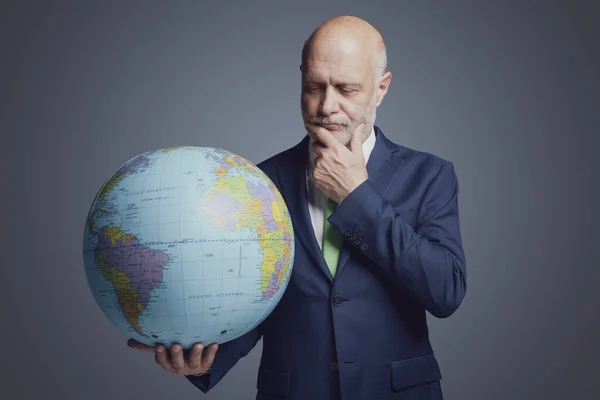 Corporate business executive holding a globe and thinking with hand on chin, global business responsibility and solutions concept