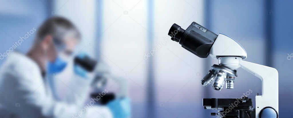 Scientist with face mask examining a sample under the microscope, scientific research concept, blank copy space