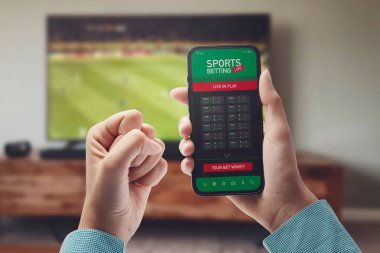 Live in-play betting app on smartphone display, a woman is betting at home and winning, POV shot