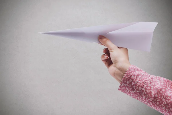 Woman holding a paper airplane and grey wall in the background, creativity and imagination concept, blank copy space