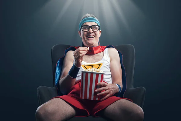 Funny happy superhero watching comedy movies and eating popcorn, he is staring at the screen and laughing