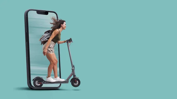 Happy young student riding an eco-friendly electric scooter, she is coming out from a smartphone screen, sustainable mobility concept