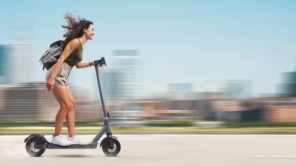 電動スクーターに乗っている幸せな屈託のない若い女性 背景の街並み — ストック写真