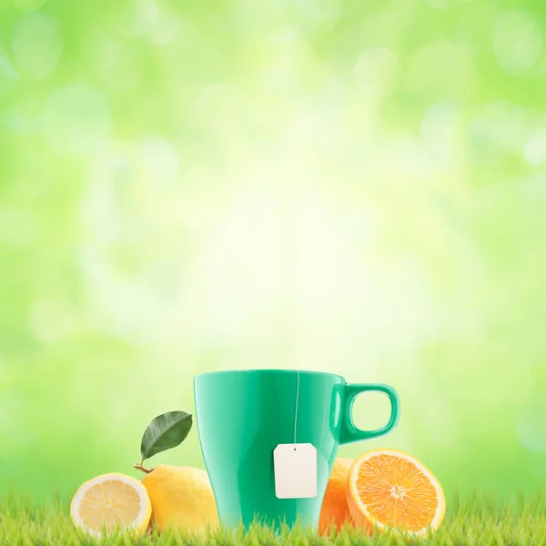 Tea brewing in a cup and citrus fruits on the grass, healthy natural tea concept