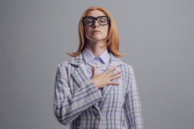 Göğsüne dokunan ve milli marşı söyleyen vatansever bir kadın, gri arka planda soyutlanmış.