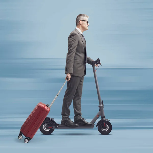 Businessman travelling and carrying his luggage, he is riding an eco-friendly electric scooter, sustainable mobility concept