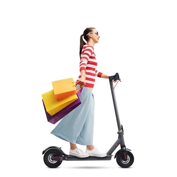 ショッピングバッグを保持し 白い背景に隔離された電動スクーターに乗るファッショナブルな女性 — ストック写真