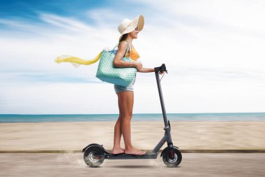 Tatilde mutlu bir kadın, elektrikli scooter kullanıyor ve plaja gidiyor.