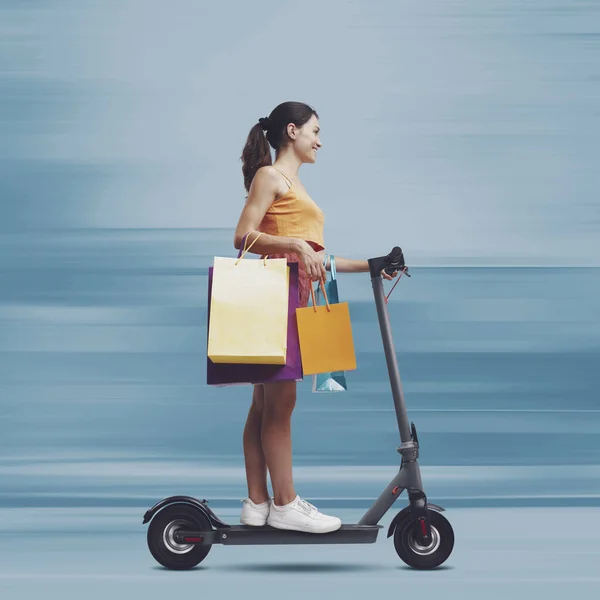 若い女性は 多くのショッピングバッグを保持し 高速電動スクーターに乗って 彼女はショッピングスプレーに起こっている — ストック写真