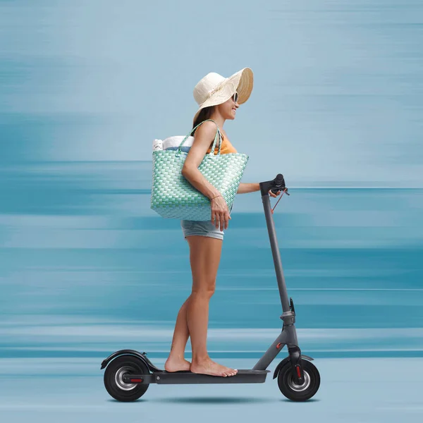 Young female tourist riding a fast eco-friendly electric scooter and going to the beach, sustainable mobility concept