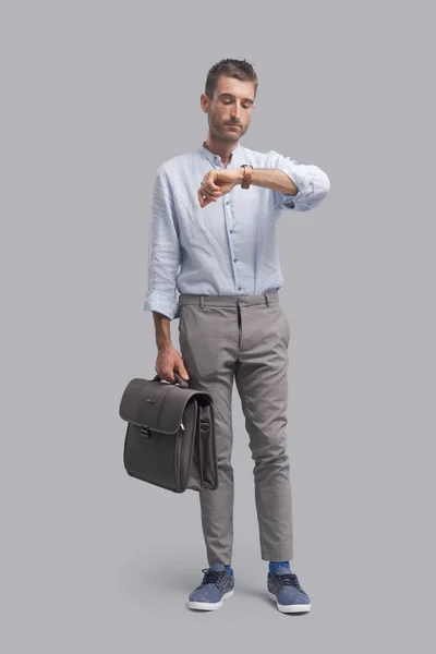 Corporate businessman standing and holding a briefcase, he is checking the time and waiting for a meeting