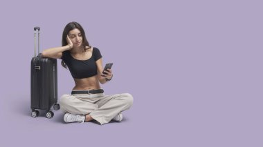 Gezgin kadın akıllı telefonuyla bağlantı kuruyor, oturuyor ve mola veriyor.