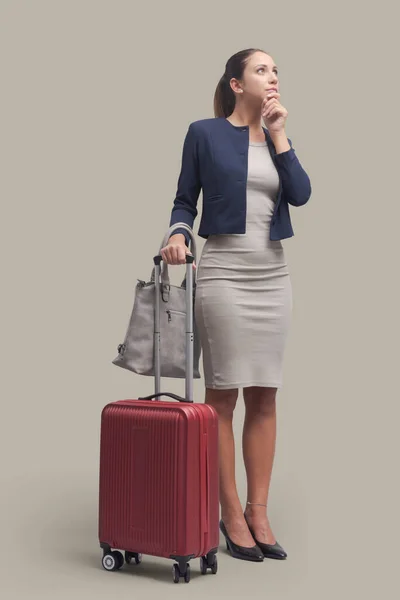 バッグやトロリースーツケースと一緒に一人旅のエレガントなビジネス女性 彼女はあごに手で考えています — ストック写真