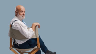 Yönetmen koltuğunda oturan ve kameraya bakan kendinden emin profesyonel film yapımcısı: drama okulu, video yapımı ve film endüstrisi konsepti, boş kopya alanı