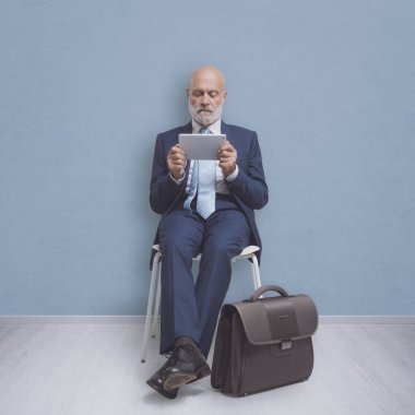 İş adamı bekleme odasında oturuyor ve tabletine bağlanıyor.
