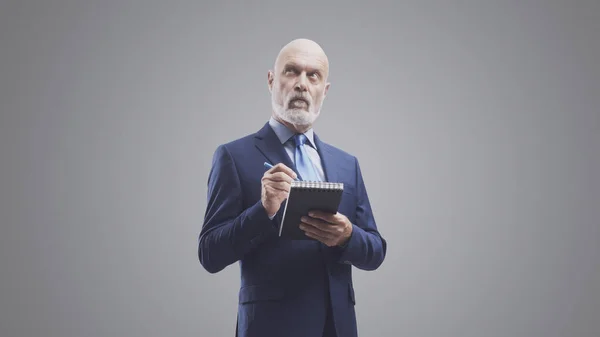 Business executive writing down notes and to do lists on a notebook, isolated on gray background