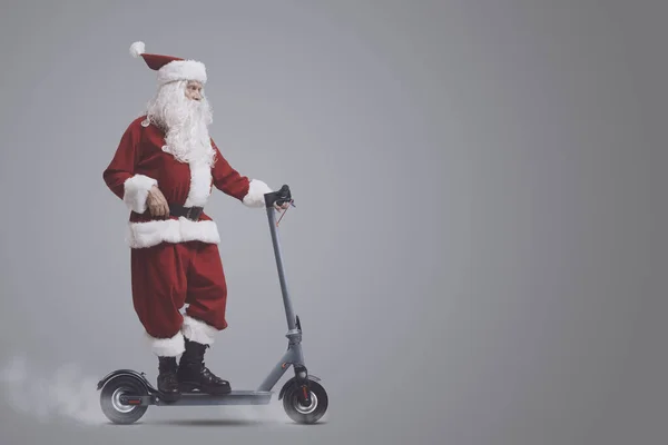 自信的当代圣诞老人骑着环保的电子摩托车 与灰色的背景隔离 空白的复制空间 — 图库照片