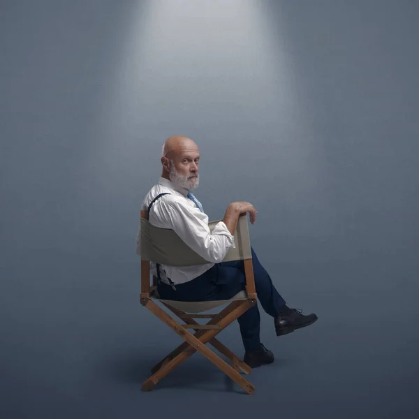 Confident film director sitting on the director\'s chair and looking at camera: video production, filmmaking and film industry concept