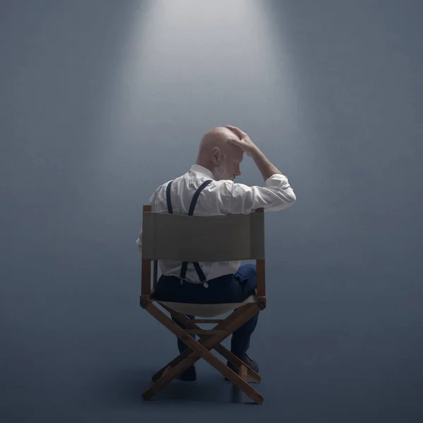失望的电影人坐在导演的椅子上 触摸着他的头 他很紧张 也很绝望 回头看 — 图库照片