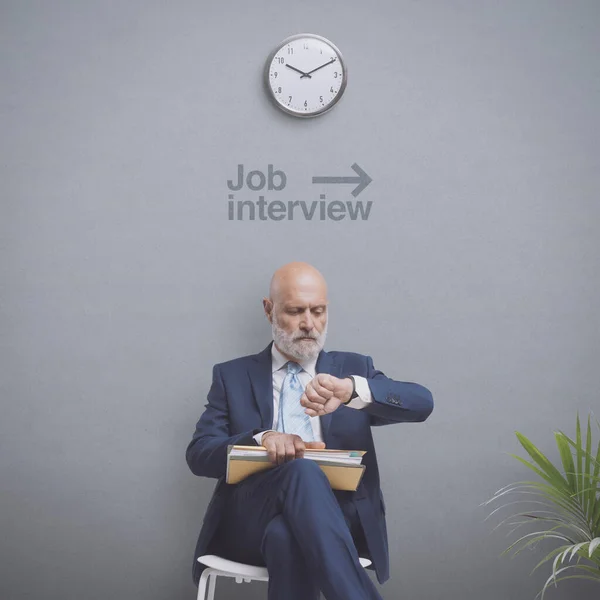 Job applicant sitting and waiting for the job interview, he is checking the time