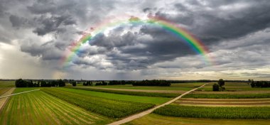 Tarlaların üzerinde gökkuşağı olan kara fırtınalı bulut - hava aracı panoraması