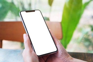 Elinde siyah cep telefonu olan, boş ekranlı, ahşap sehpada kahve fincanı olan bir kadının görüntüsü.