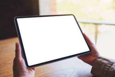 Ahşap masada beyaz ekranlı siyah tabletli bir kadının görüntüsü.