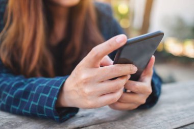 Kapalı alanda cep telefonunu tutan, kullanan ve ona bakan bir kadının yakın plan görüntüsü.