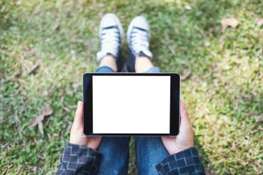Açık havada otururken boş beyaz masaüstü ekran ile siyah tablet tableti tutan ve kullanan bir kadının en üst görünüm görüntüsü