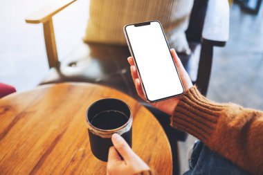 Elinde siyah cep telefonu olan, boş ekran ve kahve fincanı olan bir kadının görüntüsü. 