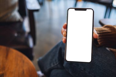 Kafede elinde siyah cep telefonu tutan ve gösteren bir kadının görüntüsü.