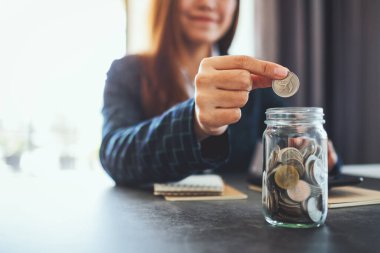 Bir iş kadınının cam kavanoza bozuk para toplayıp koyduğu yakın plan görüntüsü.