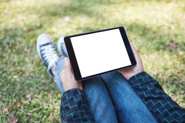 Açık havada otururken beyaz ekranlı siyah tablet tableti tutan ve kullanan bir kadının görüntüsü