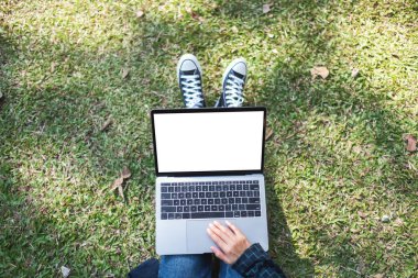 Üst görünümde, dışarıda otururken laptopta boş beyaz ekran kullanan ve yazan bir kadının görüntüsü. 