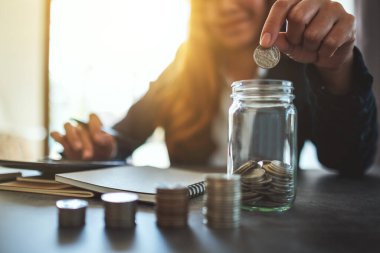 Bir iş kadınının cam kavanoza para istiflediği ve koyduğu yakın plan görüntüsü. 