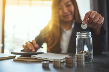 Bir iş kadınının cam kavanoza para istiflediği ve koyduğu yakın plan görüntüsü. 