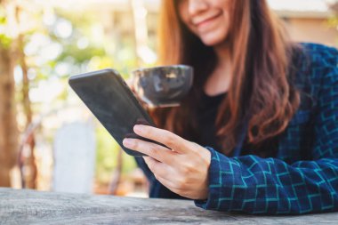 Kahve içerken cep telefonu kullanan bir kadının yakın plan görüntüsü.