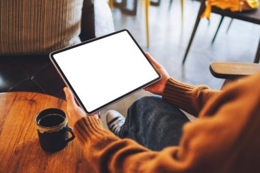 Ahşap masada beyaz ekranlı siyah tabletli bir kadının görüntüsü.