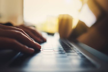 Masadaki dizüstü bilgisayarda çalışan ve yazan bir kadının ellerinin yakın plan görüntüsü.