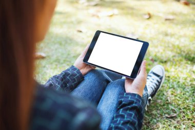 Açık havada otururken beyaz ekranlı siyah tablet tableti tutan ve kullanan bir kadının görüntüsü