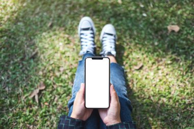 Açık havada otururken elinde boş beyaz ekran ile siyah cep telefonu tutan bir kadının en üstteki görüntüsü