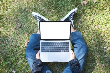 Üst görünümde, dışarıda otururken laptopta boş beyaz ekran kullanan ve yazan bir kadının görüntüsü.