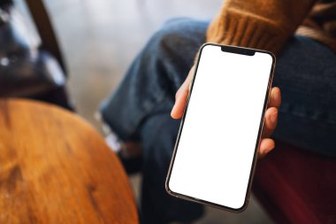 Kafede elinde siyah cep telefonu tutan ve gösteren bir kadının görüntüsü.