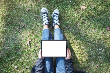 Açık havada otururken boş beyaz masaüstü ekran ile siyah tablet tableti tutan ve kullanan bir kadının en üst görünüm görüntüsü