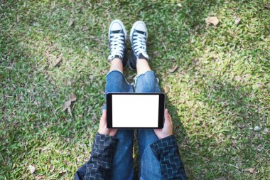 Açık havada otururken boş beyaz masaüstü ekran ile siyah tablet tableti tutan ve kullanan bir kadının en üst görünüm görüntüsü