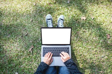 Üst görünümde, dışarıda otururken laptopta boş beyaz ekran kullanan ve yazan bir kadının görüntüsü.